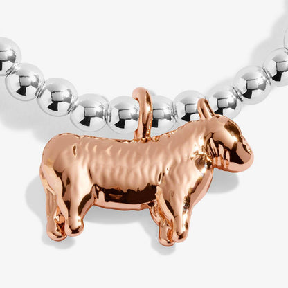 A close-up of a metallic cow-shaped pendant in rose gold, hanging from a strand of polished silver beads on a light gray background.