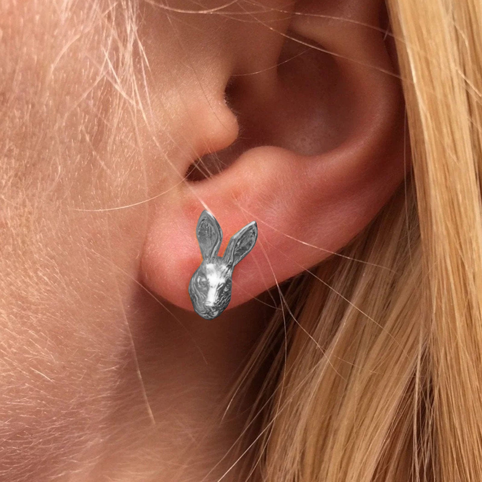 A close-up of a person's ear wearing a small silver bunny stud earring.