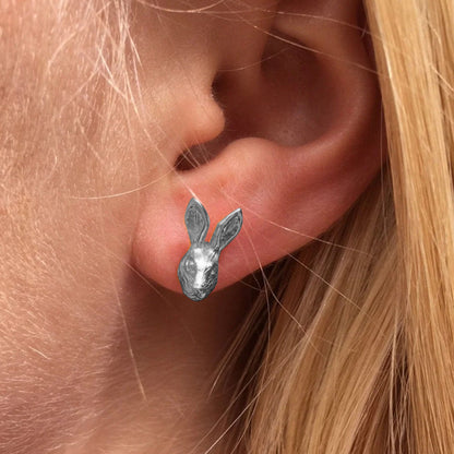 A close-up of a person's ear wearing a small silver bunny stud earring.