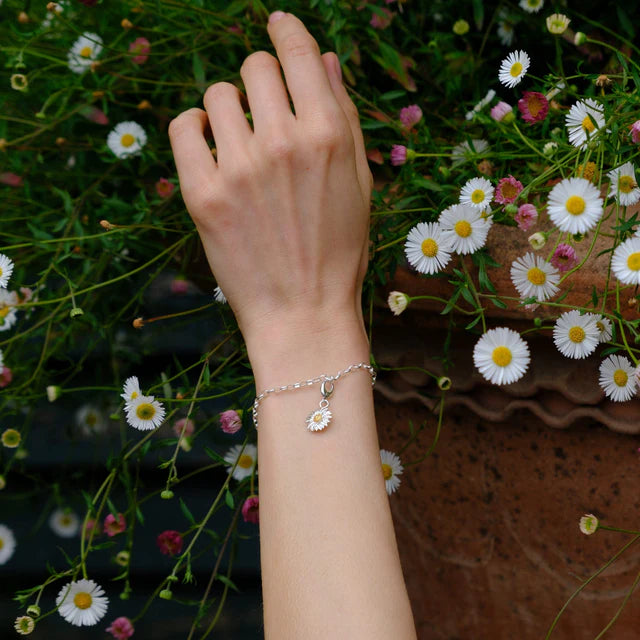 Hand wearing a silver bracelet with a flower charm against a floral background