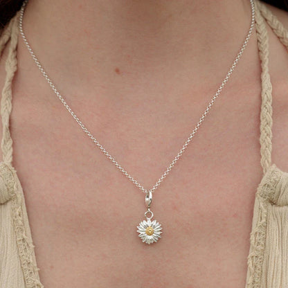 Silver necklace with a daisy pendant on a person wearing a beige top.