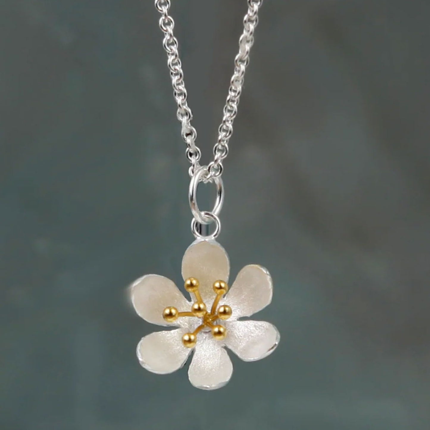Floral pendant necklace with gold accents on a chain against a dark background