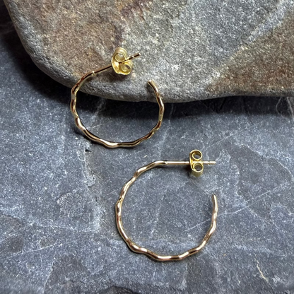 Gold hoop earrings on a stone surface