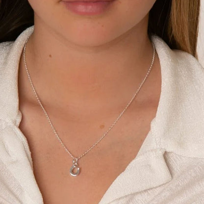A close-up of a person wearing a delicate silver chain necklace with a small horseshoe pendant, styled with a white textured collared shirt.