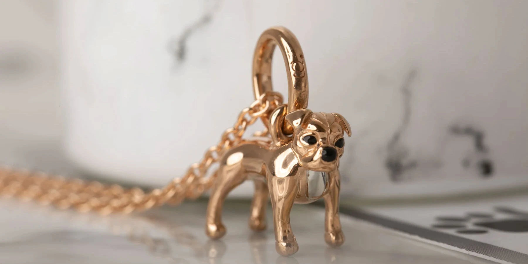 Gold dog-shaped pendant on a chain against a marble background