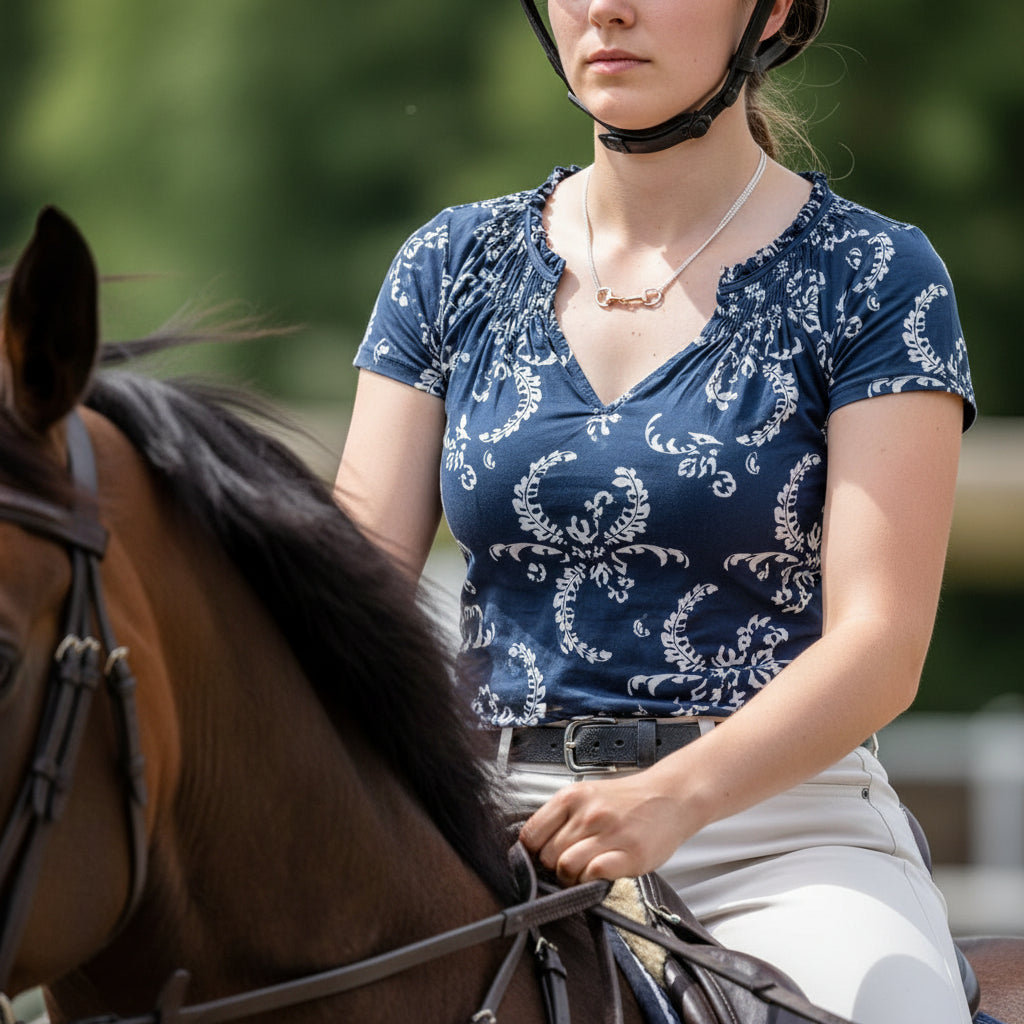 Woman in a blue patterned shirt sitting on a horse with a blurred green background