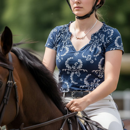 Woman in a blue patterned shirt sitting on a horse with a blurred green background