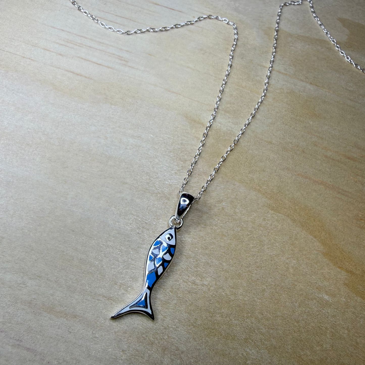 Fish-shaped pendant on a chain against a beige background