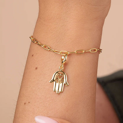 Gold bracelet with a hamsa hand charm on a wrist against a beige background