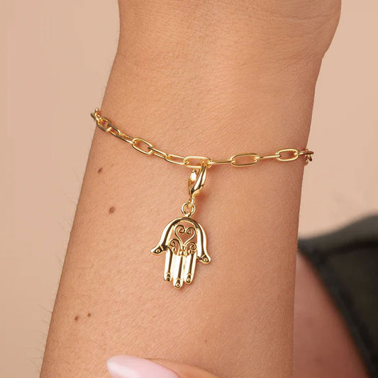 Gold bracelet with a hamsa hand charm on a wrist against a beige background