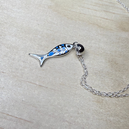 Fish-shaped pendant on a chain against a light wood background