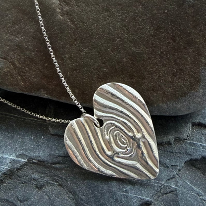 Heart-shaped silver pendant on a chain against a stone background