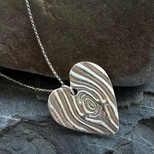 Heart-shaped silver pendant on a chain against a stone background