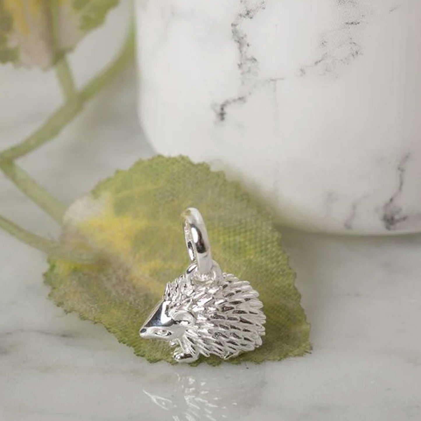 Silver hedgehog charm on a green leaf with a marble background