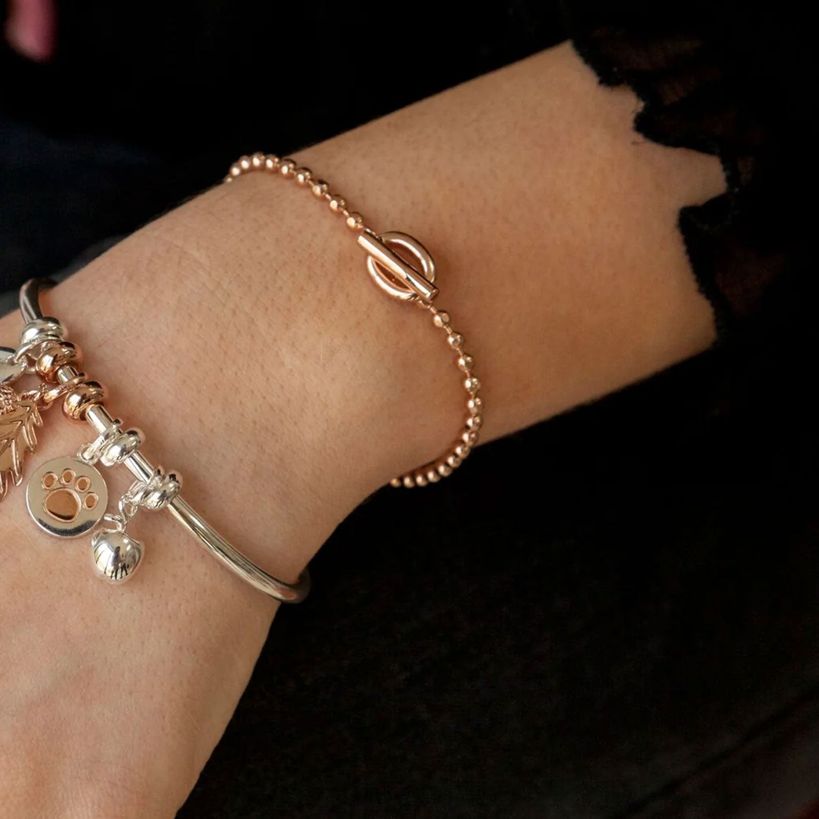 Close-up of a wrist wearing a gold bracelet with charms on a dark background