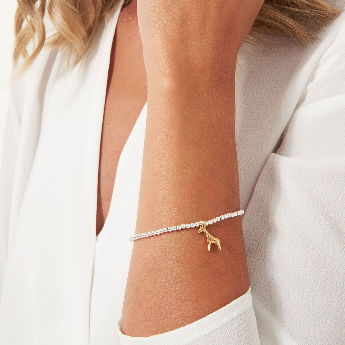 Gold bracelet with a small giraffe charm on a person's wrist against a white background
