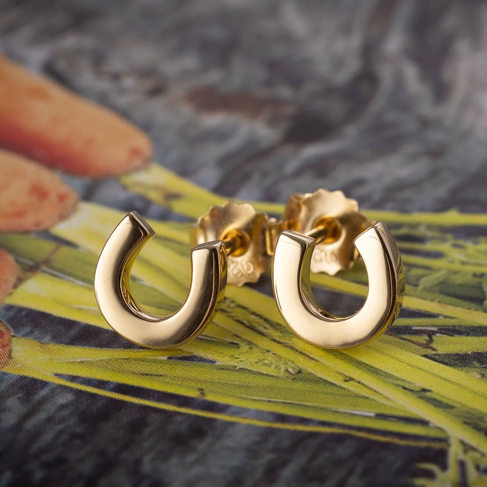 Gold hroseshoe earrings on a textured surface with a blurred background