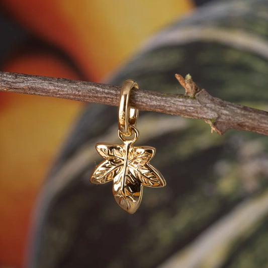 Gold leaf-shaped pendant on a branch with a blurred natural background
