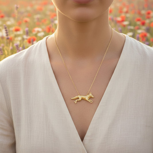 Gold fox pendant necklace on a person in a field of flowers