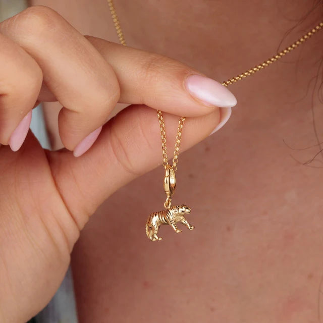 Gold necklace with a zebra pendant held by a hand against a neutral background