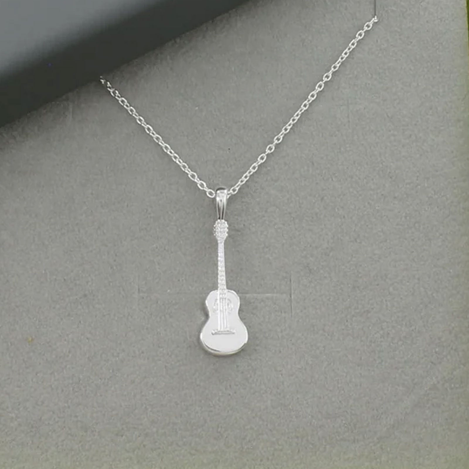 Silver guitar-shaped pendant on a chain against a gray background