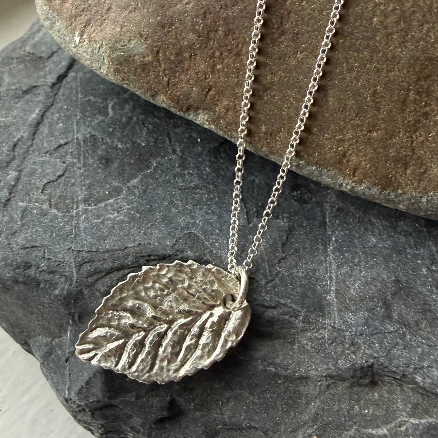 Silver leaf pendant necklace on a stone surface