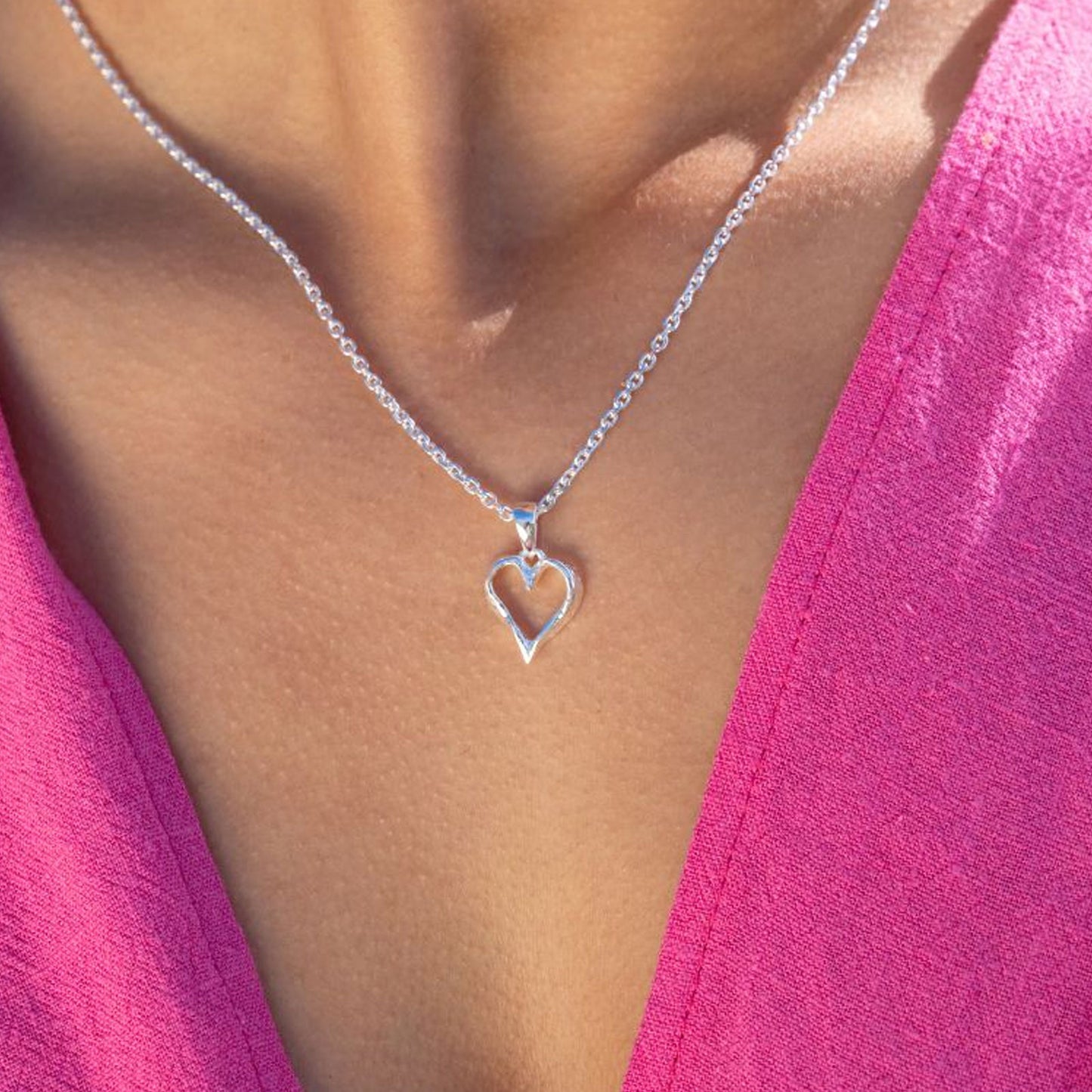 Silver heart-shaped necklace on a person wearing a pink top