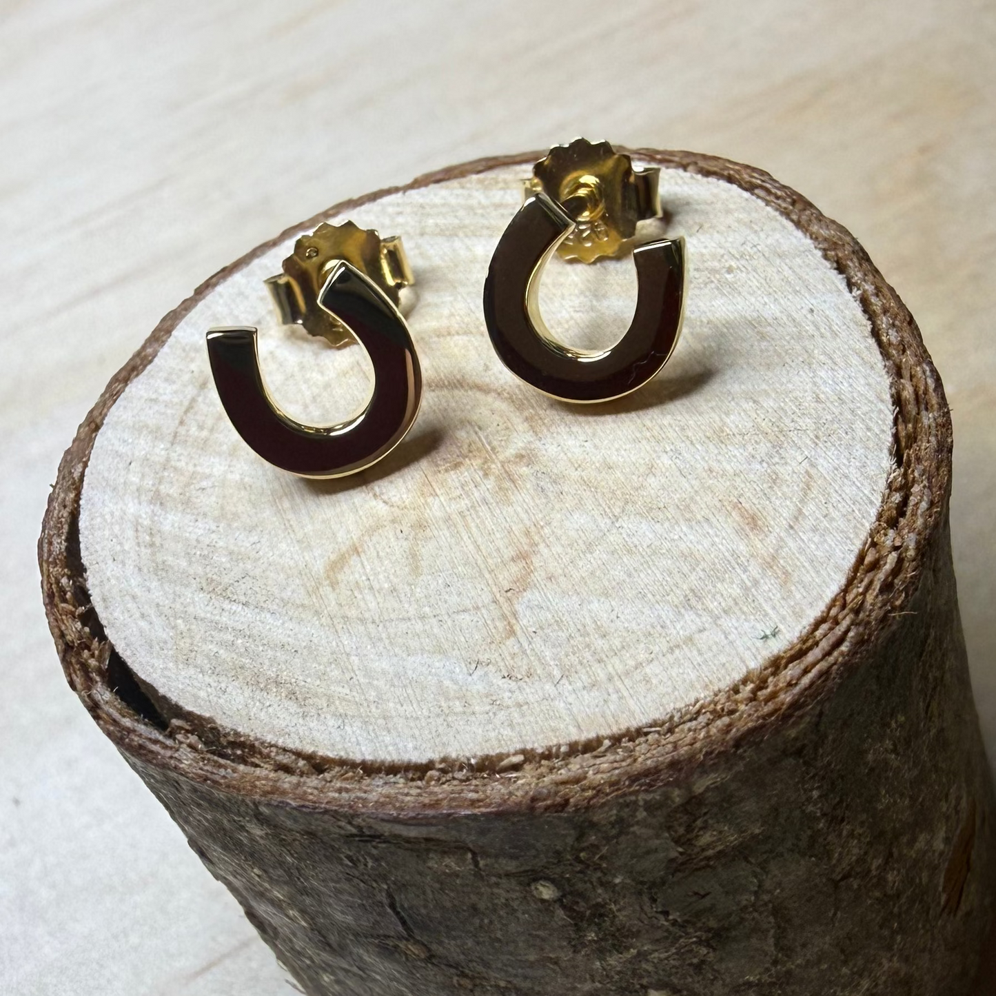 Pair of gold horseshoe earrings on a wooden stand with a white cloth on a light brown surface.