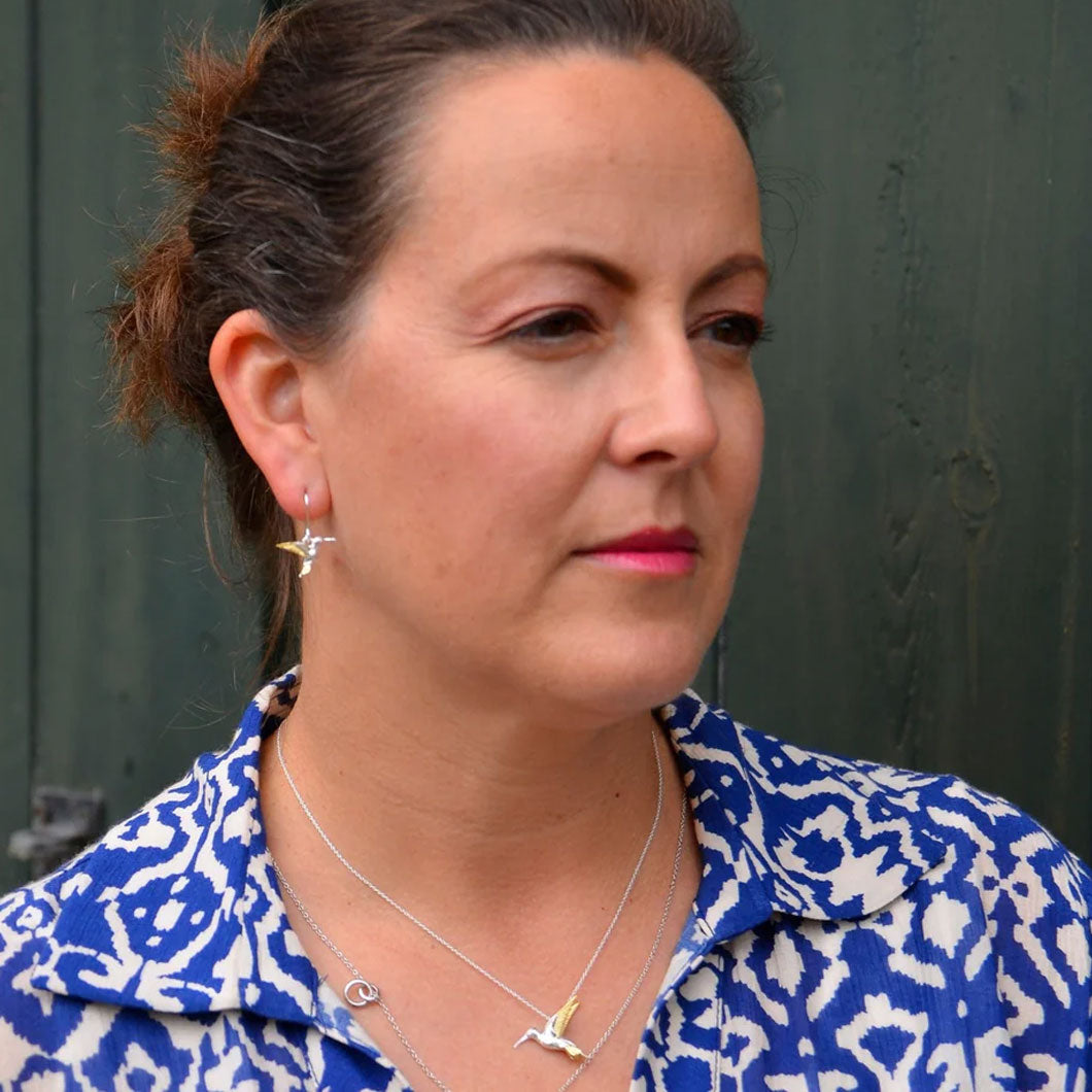 Woman wearing a blue and white patterned shirt with hummingbird drop earrings
