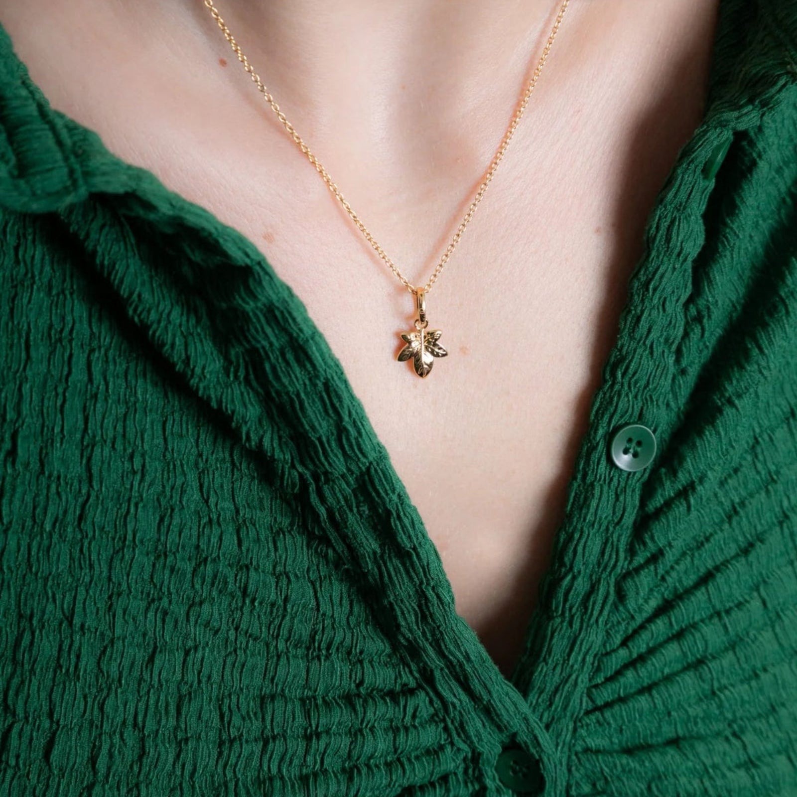 Close-up of a person wearing a gold necklace with a pendant, against a green garment.