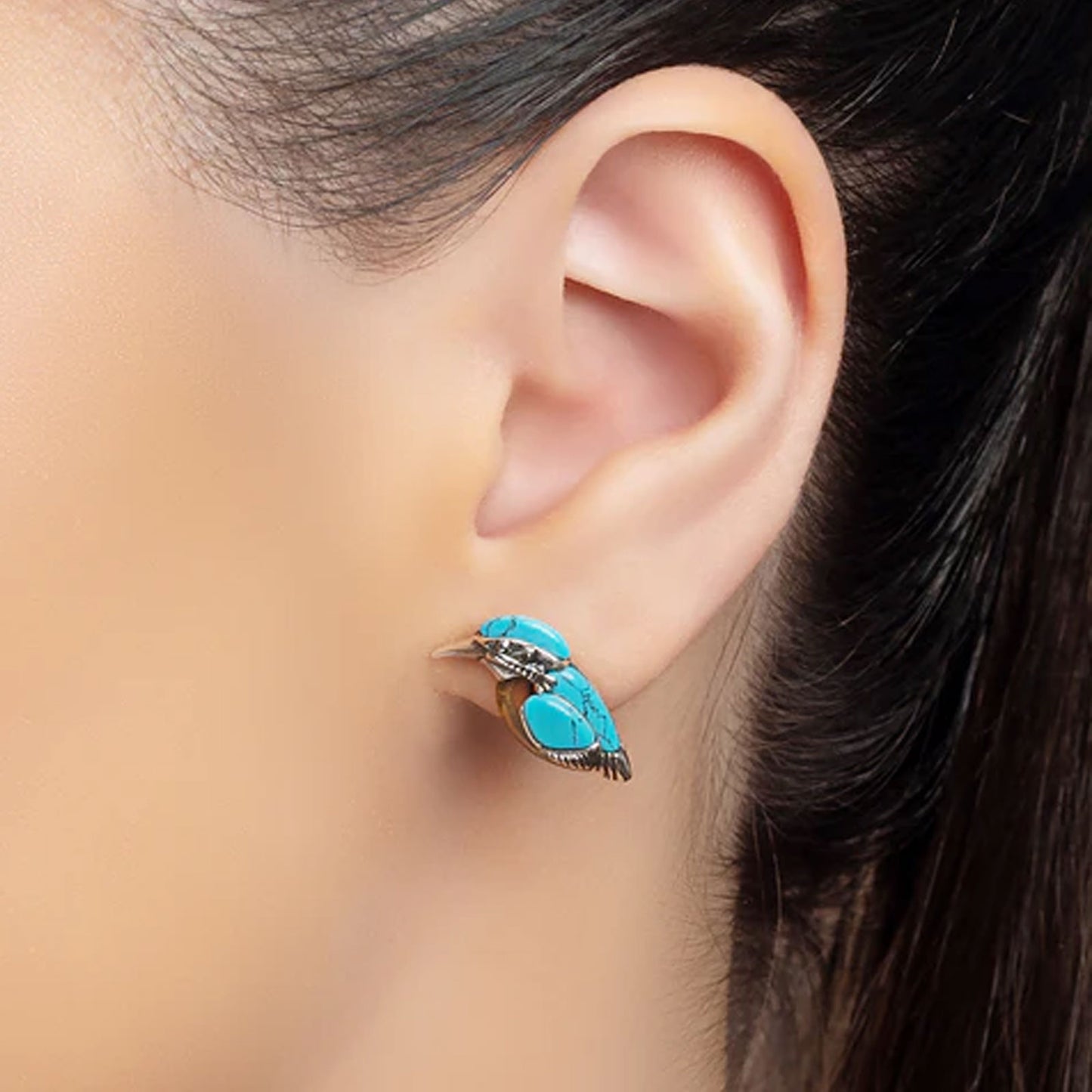 Close-up of an ear wearing a turquoise earring with a blurred background