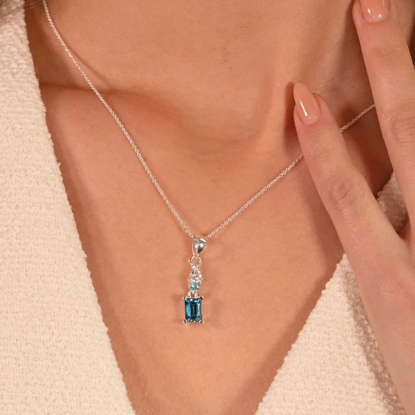 Necklace with a blue gemstone pendant being worn and adjusted by a hand.