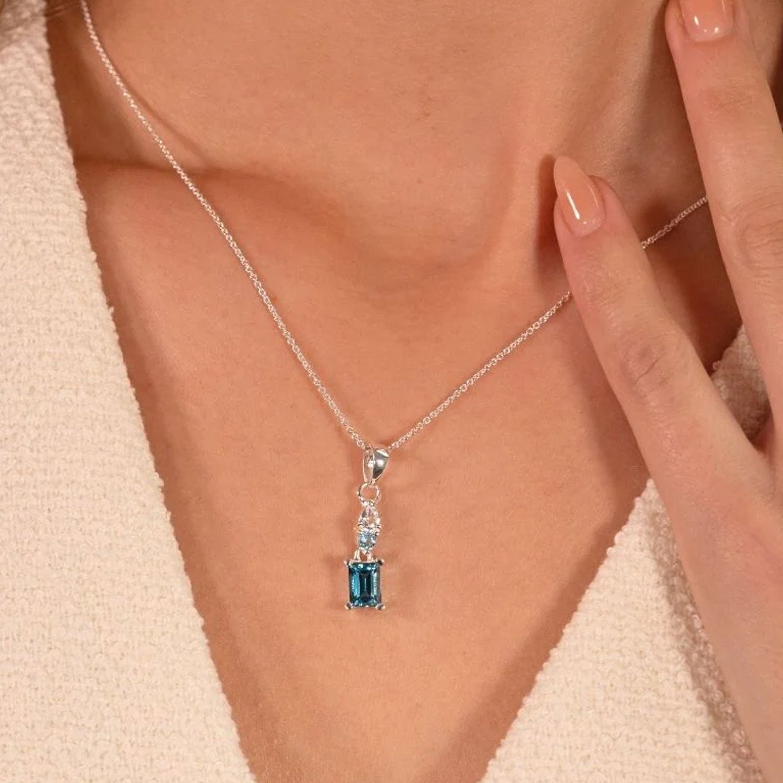 Necklace with a blue gemstone pendant being worn and adjusted by a hand.