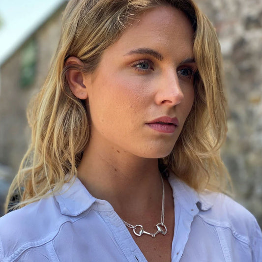 Woman wearing a silver necklace with a heart-shaped pendant against a blurred background