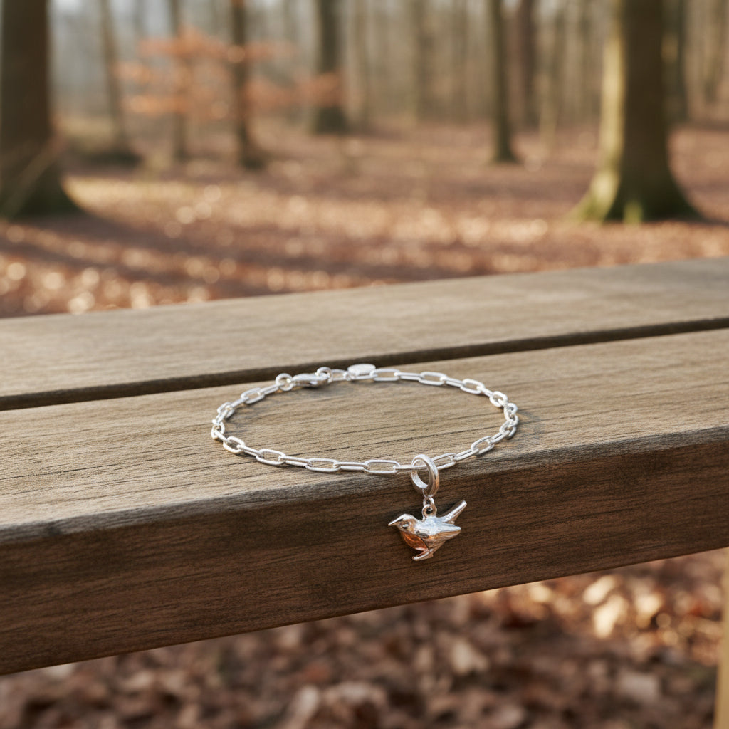 Silver chain bracelet with a bird charm on a bench in a wood