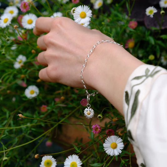 Hand wearing a silver bracelet with daisy charms in a floral setting