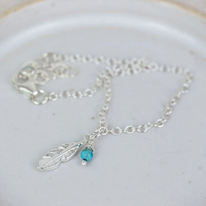 Silver necklace with feather and turquoise bead charm on a white plate