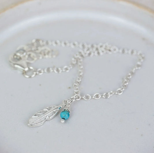 Silver necklace with feather and turquoise bead charm on a white plate