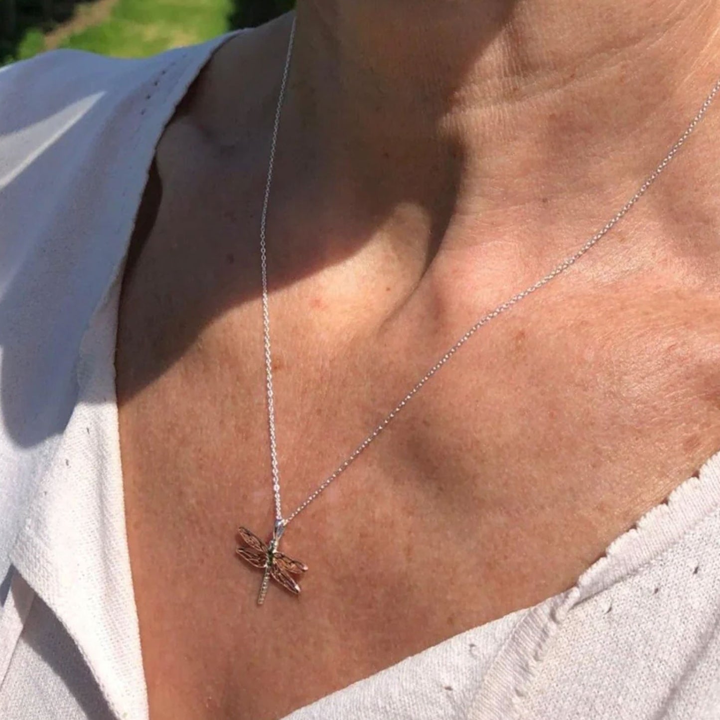 Close-up of a necklace with a dragonfly pendant on a person's neck.