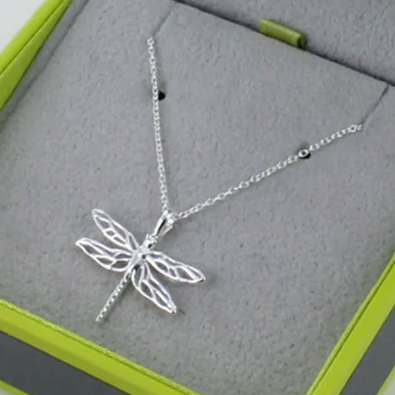 Silver dragonfly necklace on a gray surface with green edges