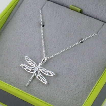 Silver dragonfly necklace on a gray surface with green edges
