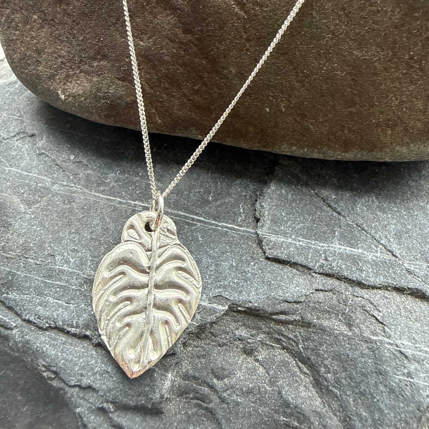 Silver leaf pendant necklace on a stone surface