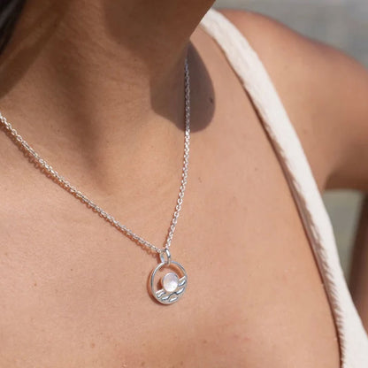 A close-up of a person wearing a delicate silver chain necklace with a circular pendant featuring a small white moon, paired with a white top.
