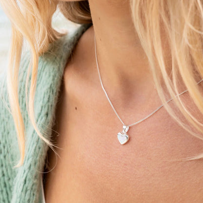 Silver heart-shaped pendant necklace on a person wearing a light green sweater.