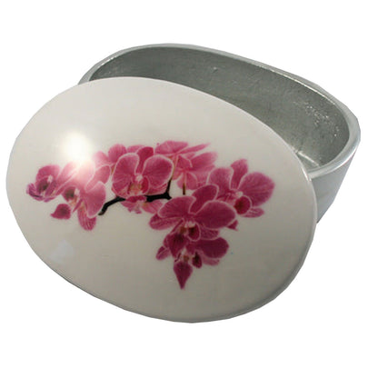 An oval-shaped white ceramic box with a glossy finish, featuring a painted pink orchid design on the lid. The box is shown open, revealing a silver-toned interior, set against a plain white background.