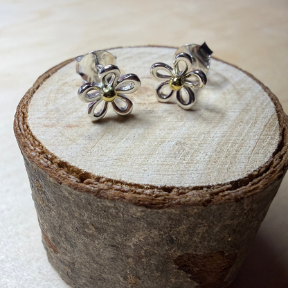 Silver flower-shaped earrings on a wooden stand with a blurred background