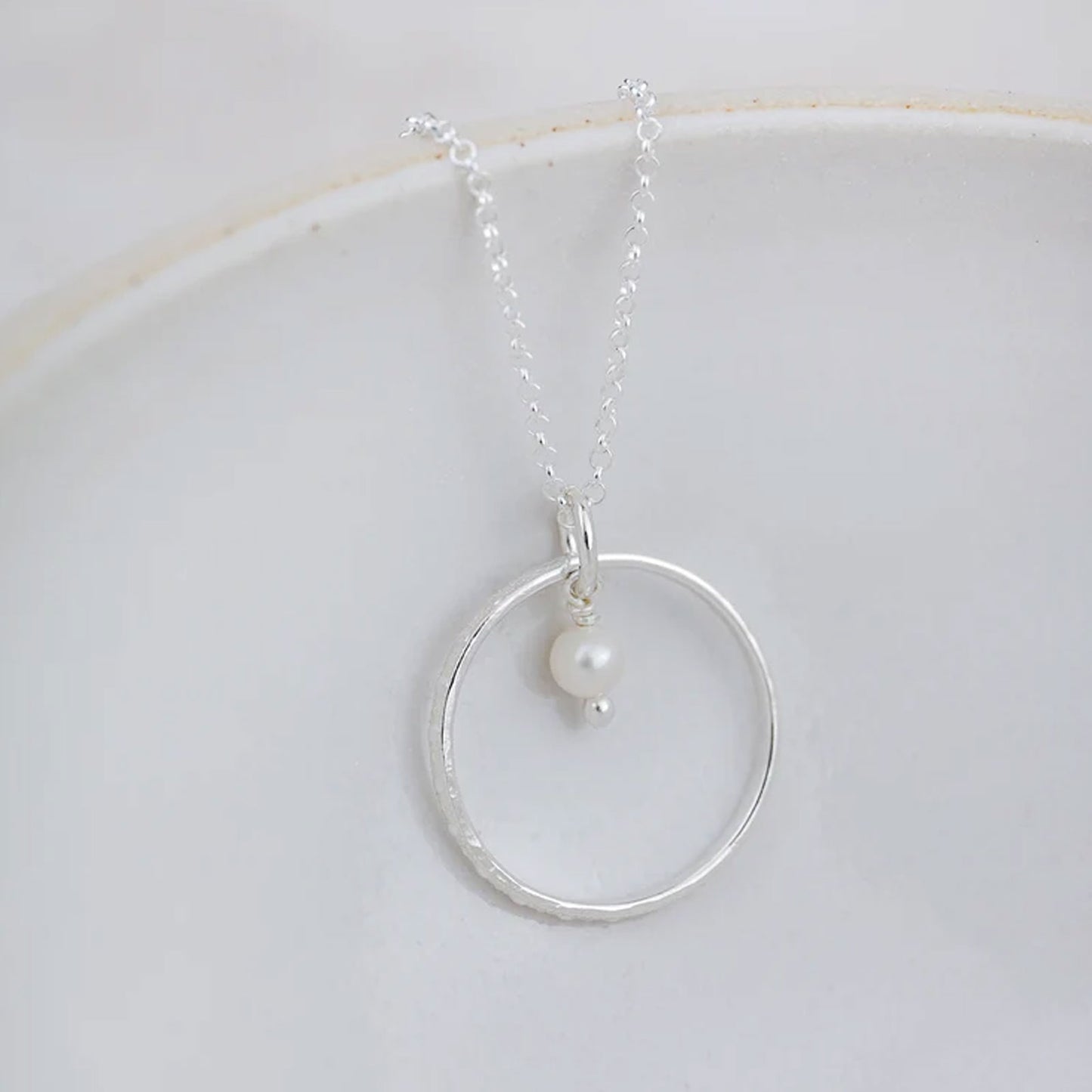 Silver necklace with a circular pendant and pearl on a white background