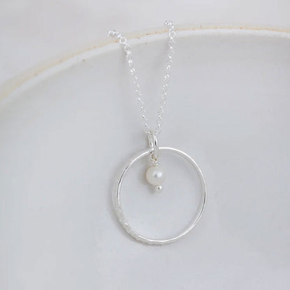 Silver necklace with a circular pendant and pearl on a white background