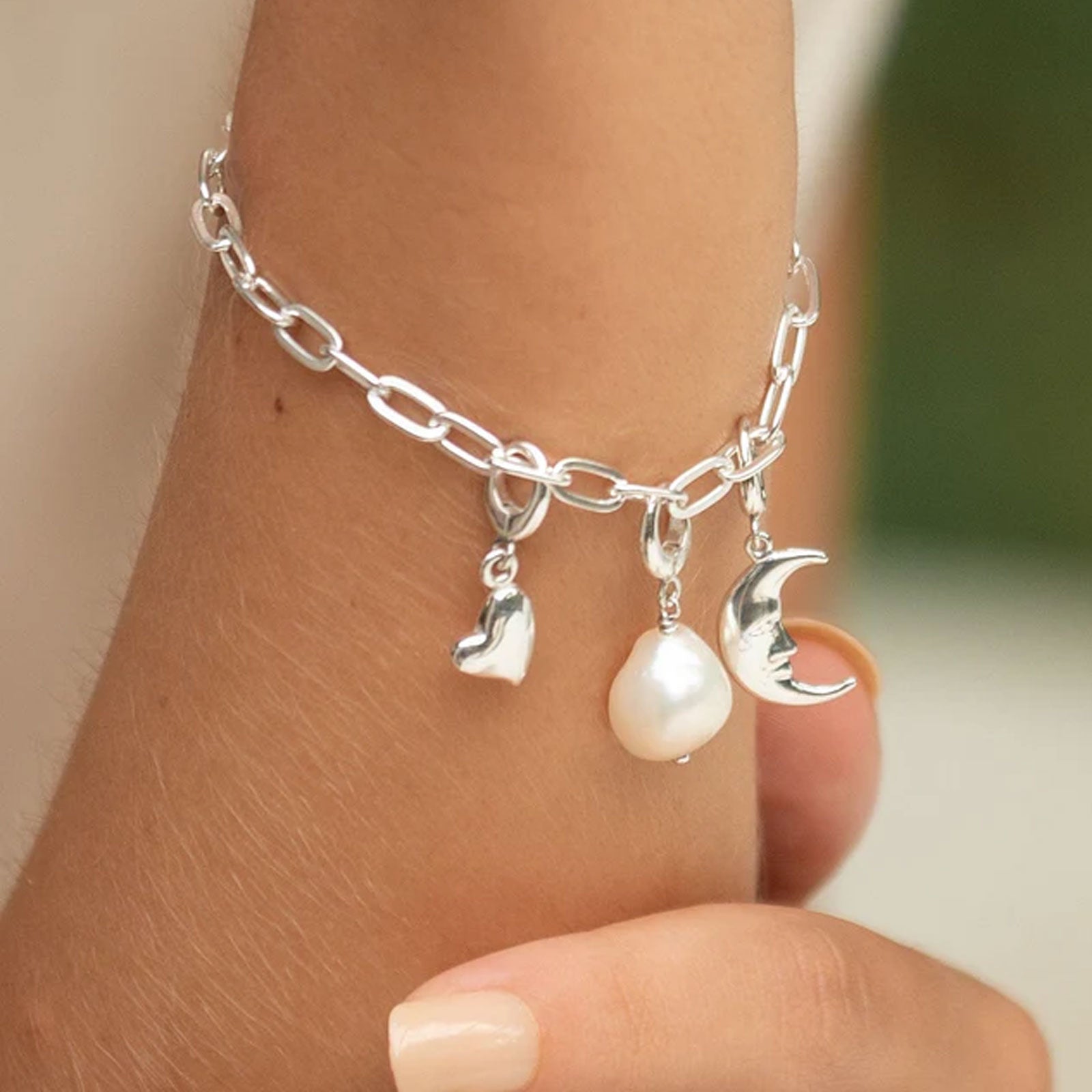 Silver anklet with heart, pearl, and moon charm on a person's ankle.