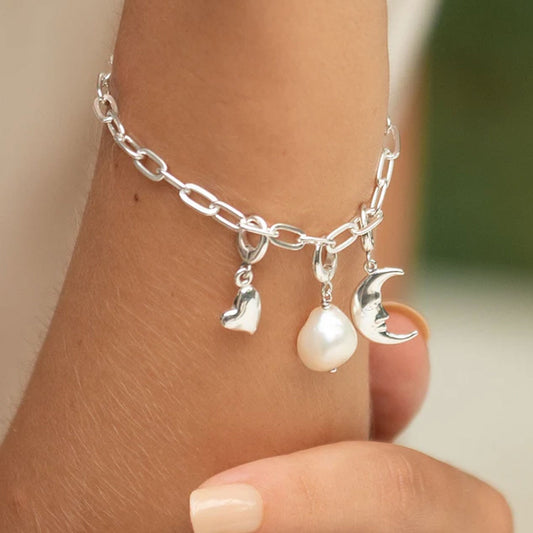 Silver anklet with heart, pearl, and moon charm on a person's ankle.